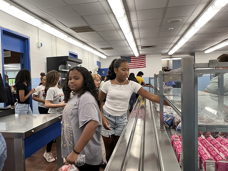 A cafeteria line with middle school girls selecting snacks.