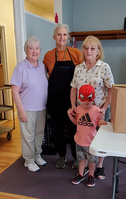 Three adults and one child, who is wearing a red spiderman mask. The person in the center is wearing a long black apron.