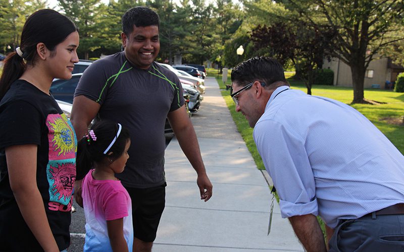 A man in a blue button-down shirt leans in as he talks to a little girl. There is a man and woman on either side of her smiling.