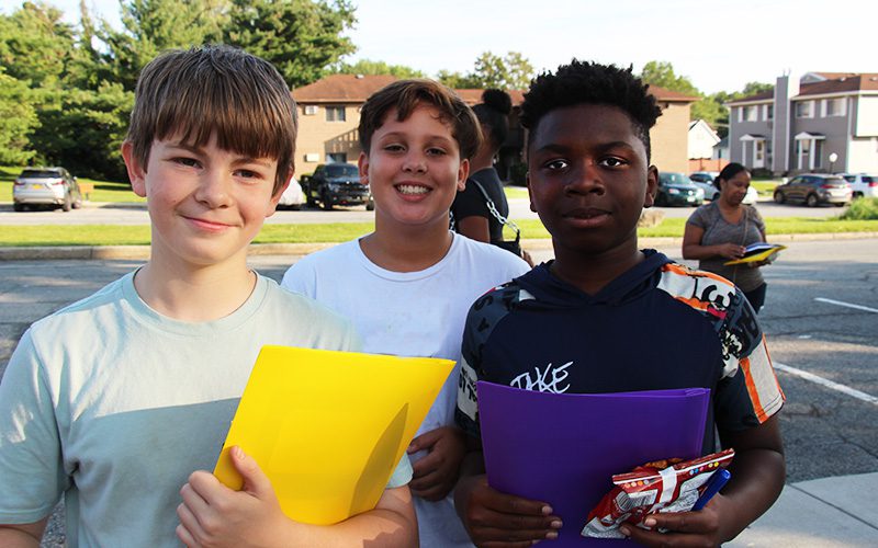 Three middle school boys stand together smiling, holding folders.