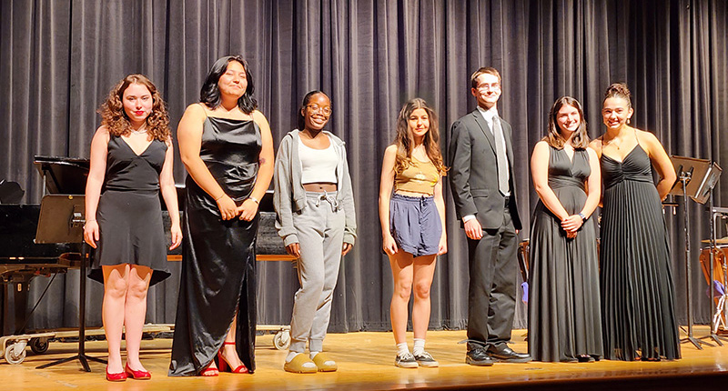 A group of seven high school and middle school students stand on a stage.