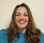 A woman with long light brown hair, wearing a blue shirt, smiles.