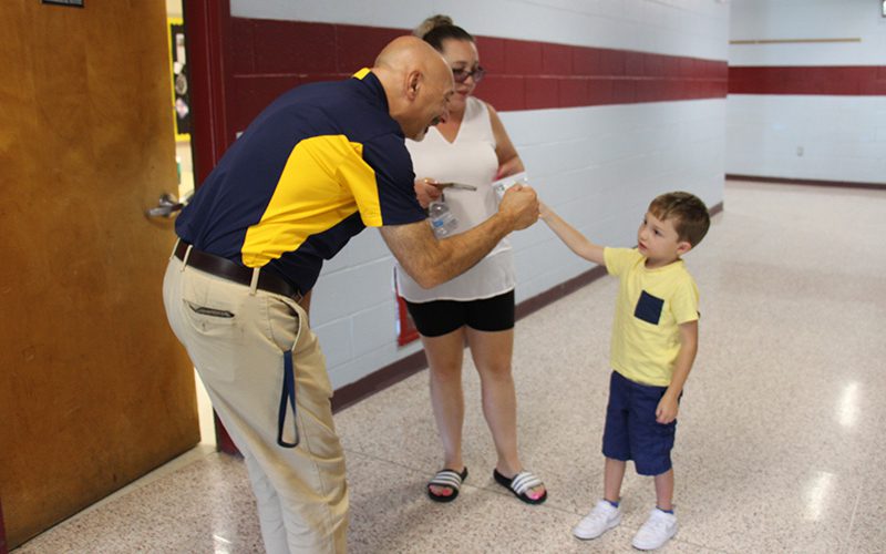 A little boy wearing a yellow shirt and blue shorts gives a fistbump to a man wearing a blue and gold shirt.