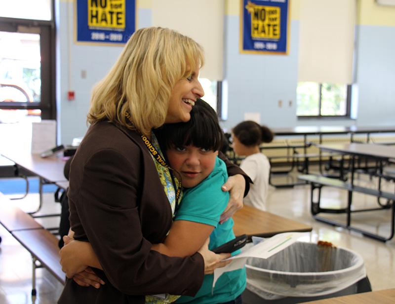 A woman in a brown suit with shoulder-length blonde hair gets a hug from a fourth-grader.
