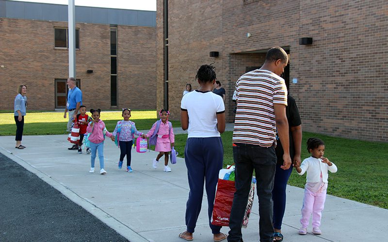 Three little girls hold hands and walk together toward three adults.