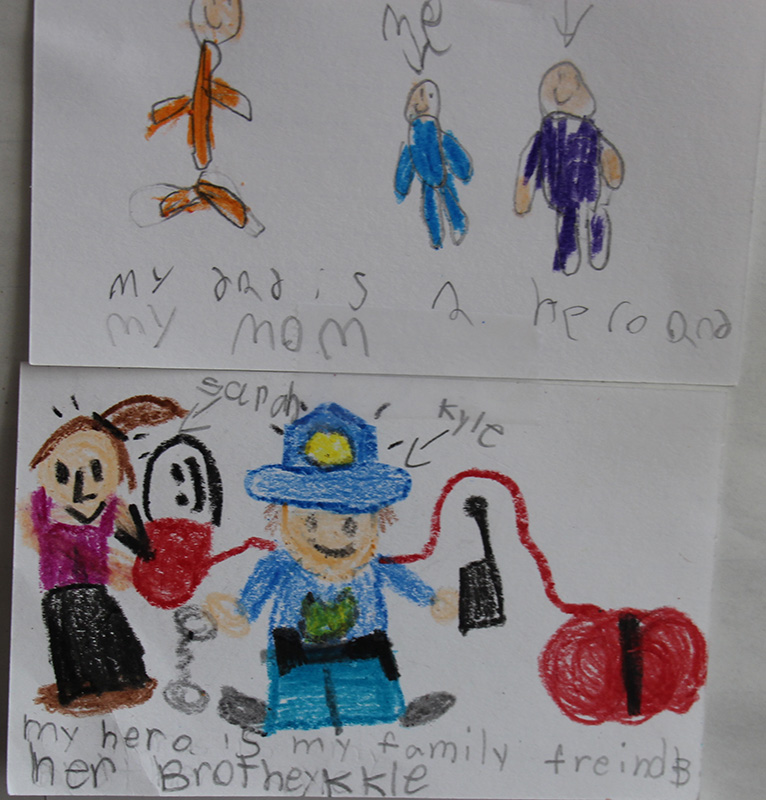 White cards with drawings of people on them drawn by third grade kids