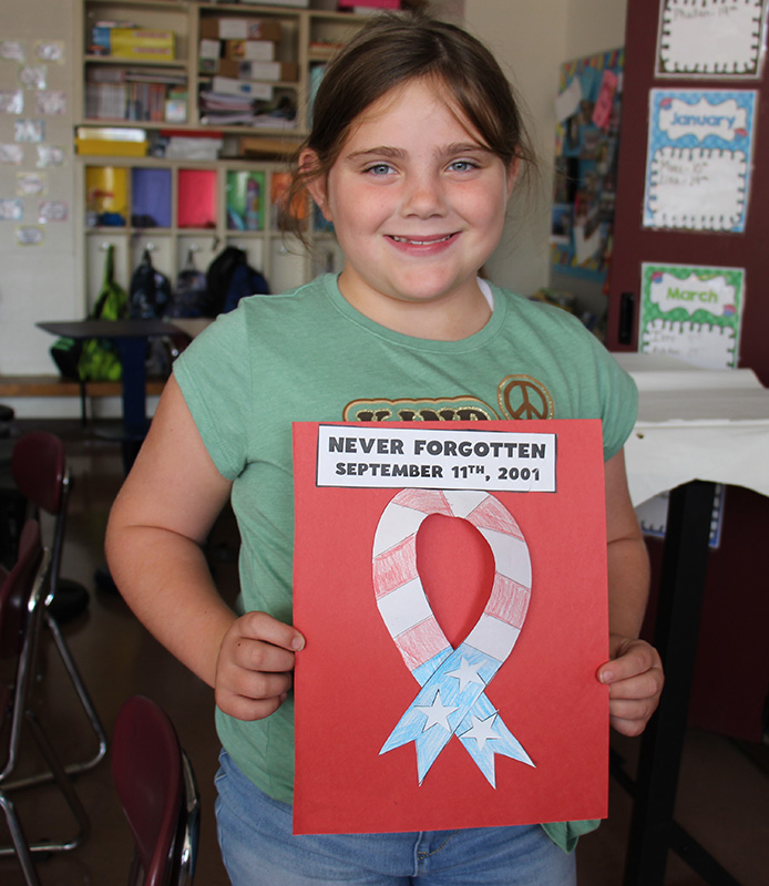 A girl smiles and holds a red piece of paper with a red white and blue cut out ribbon on it.