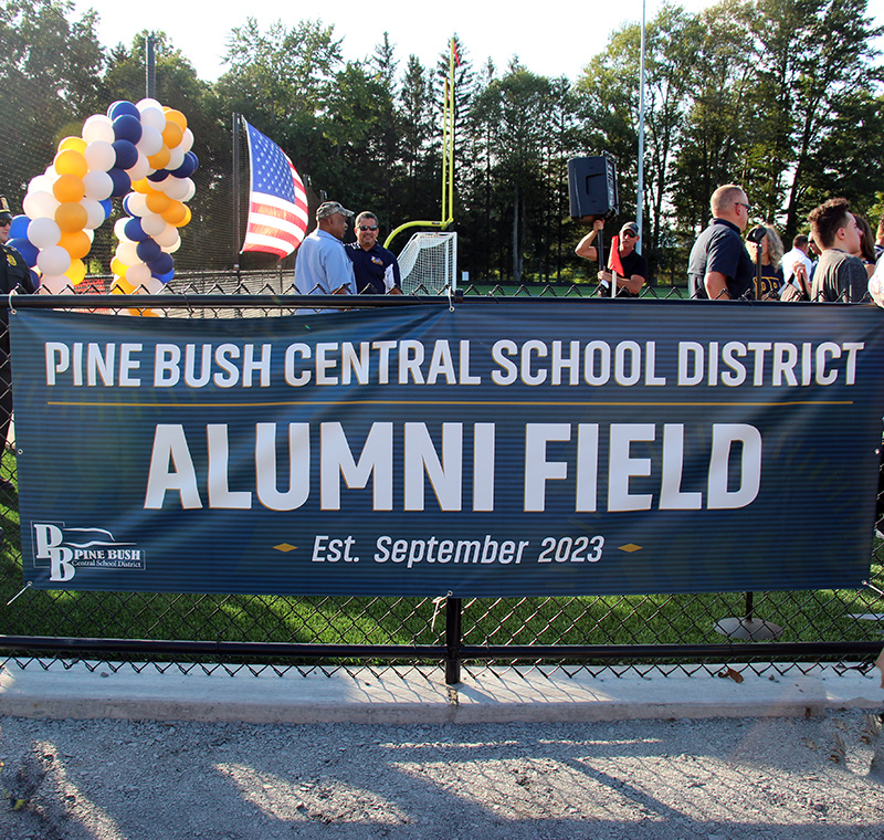 A blue sign with white lettering that says Pine Bush Central School District alumni field.