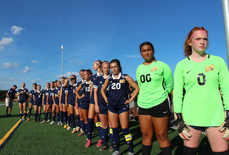 A line of high school girls all dressed in soccer uniforms.