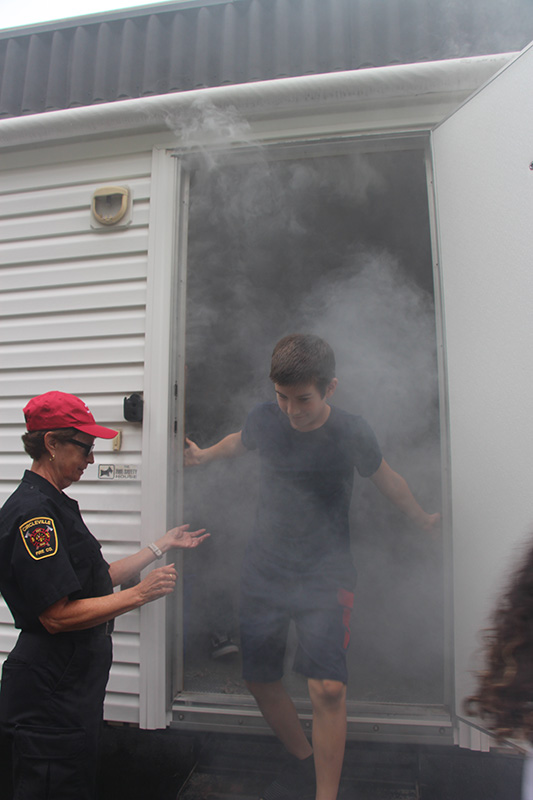 An older elementary age boy comes out of a smoky room, with the help of a firefighter.