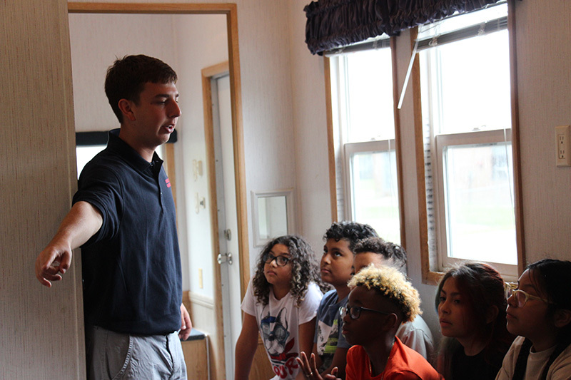 A young firefighter stands in a small room with fifth grade students, talking to them.