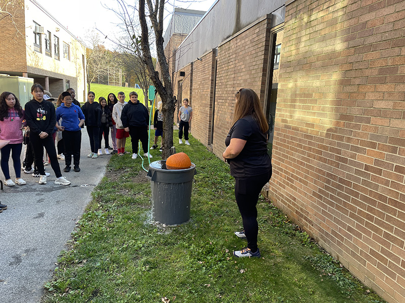 Students on the left and a woman on the right with a pumpkin sitting in a big bin of water floating.