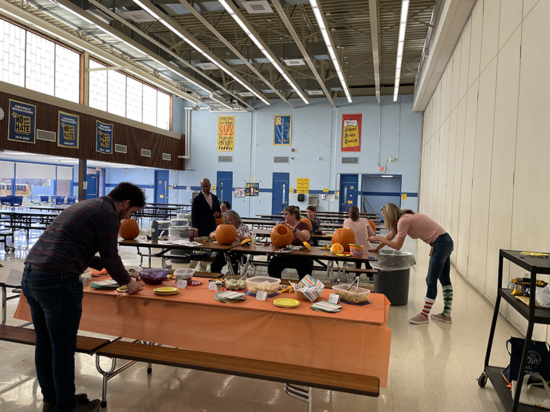 Long tables with adults sittin gat some carving pumpkins.