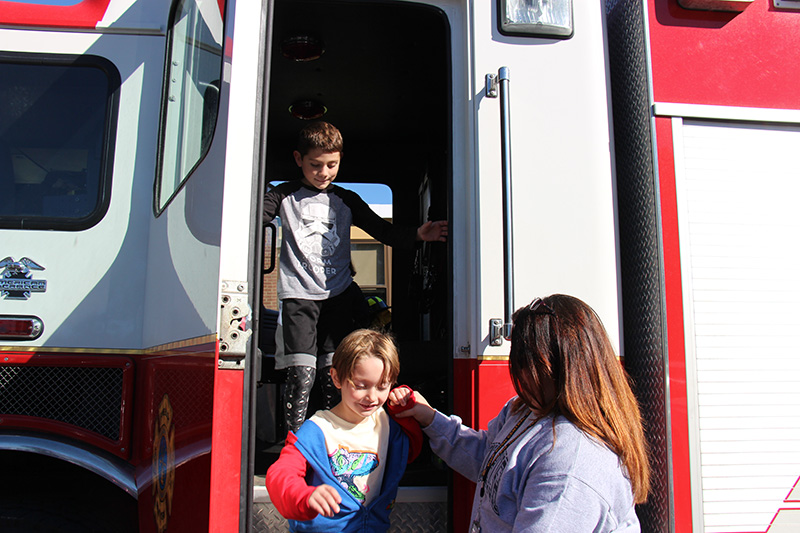 Two elementary boys come down the steps of a big fire truck.