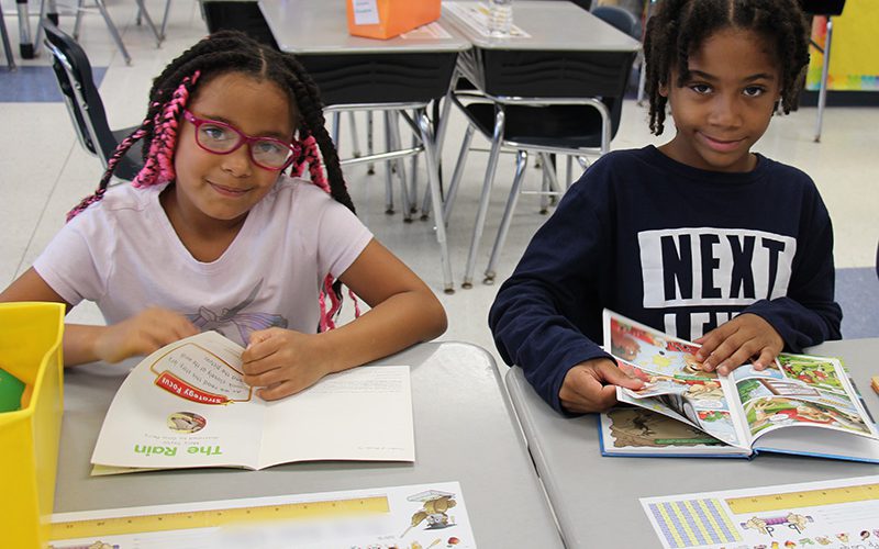 Two second grade girls sit together and read. They are smiling.