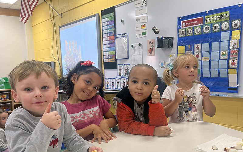 Four pre-K students taste pieces of apple. They are smiling and giving thumbs up.