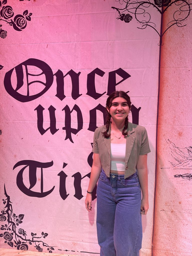 In front of a pink backdrop that says Once Upon a Time, a young woman with braids smiles.