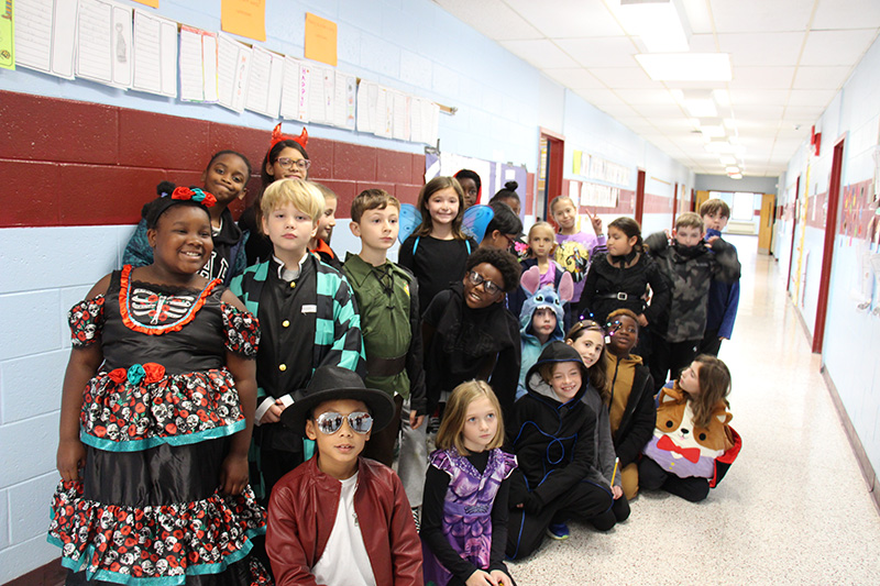 A large group of kids in a hallway, most dressed in costumes.