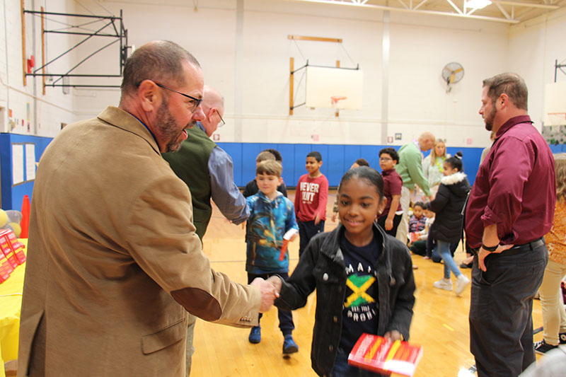 A third-grade girl wearing a black and green shirt shakes hands with a man after receive a red dictionary.