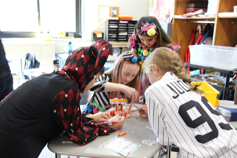 A group of four fifth-grade kids lean into the center of a desk to work together.