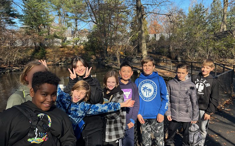 Nine sixth-grade students smile as they stand outside with trees in the background.