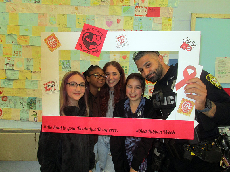 A group of four middle schools girls stand with a police officer inside a photo frame about living drug free.