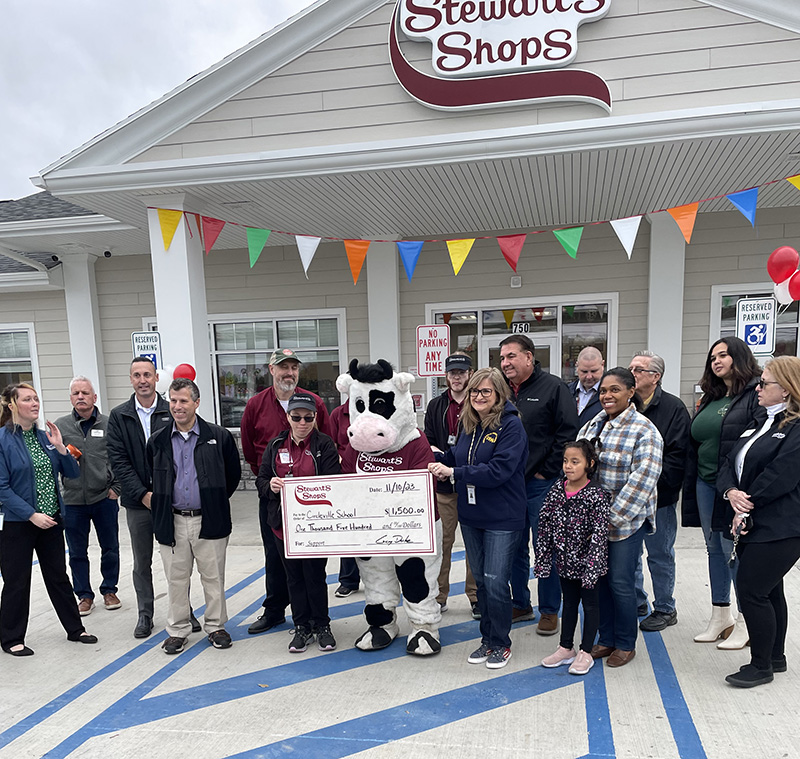 A large group of people stand outside of a store with the people in the center holding a big oversized check.