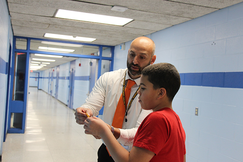 A man with a white shirt and red tie hands a piece of paper to a middle school boy.
