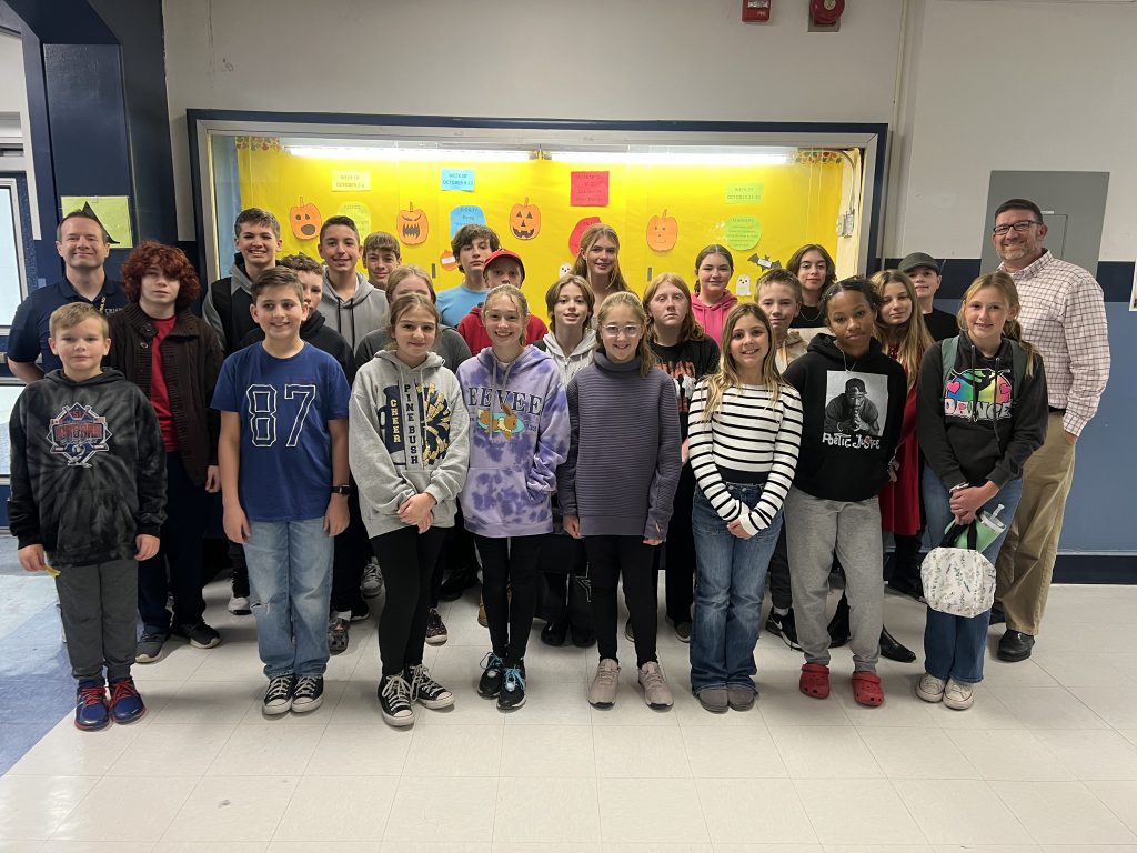 A large group of middle school students stand with two men - their principal and assistant principal.