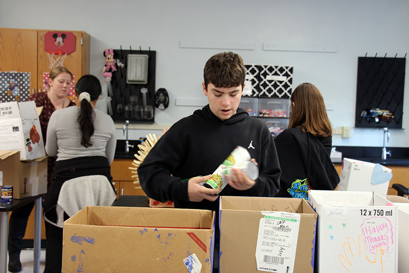 A young man with short dark hair puts canned food into boxes.