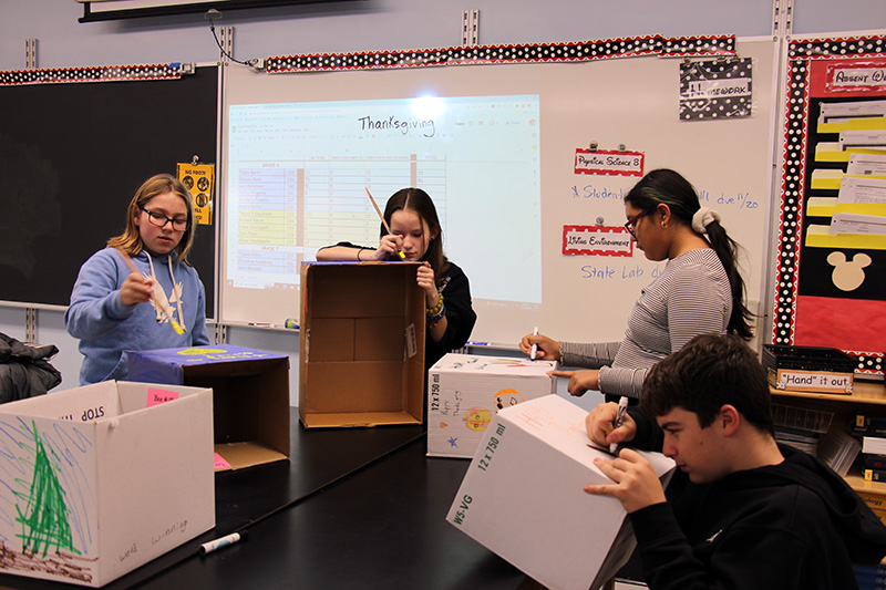 Four middle school students paint boxes for Thanksgiving.