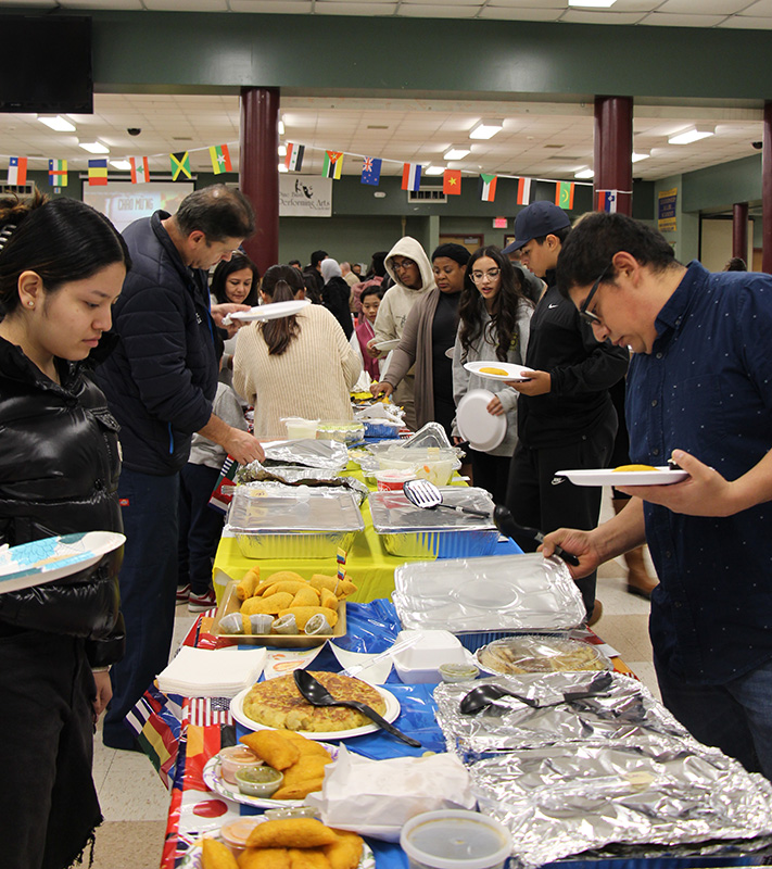 A long table filled with foods from around the world. There are lines on either side of the table as people spoon food onto their plates.