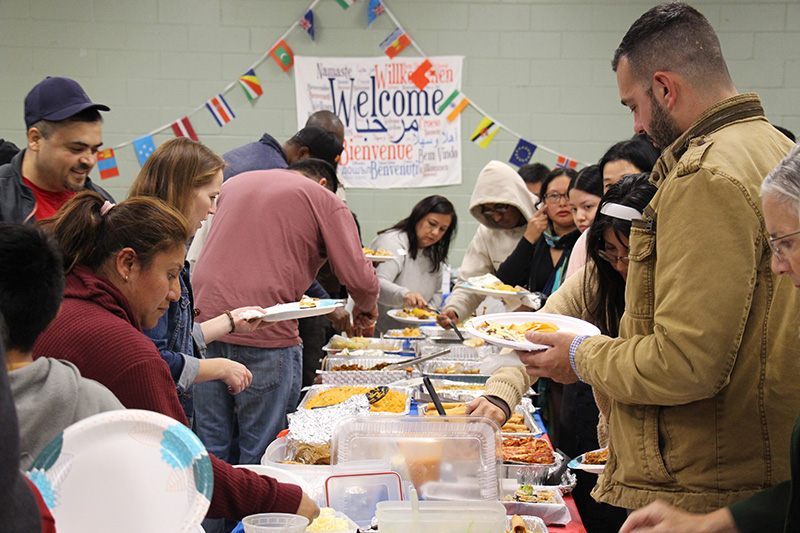 A long table filled with foods from around the world. There are lines on either side of the table as people spoon food onto their plates.