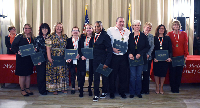 A group of 11 people, all with medals around their necks, stand holding certificates.