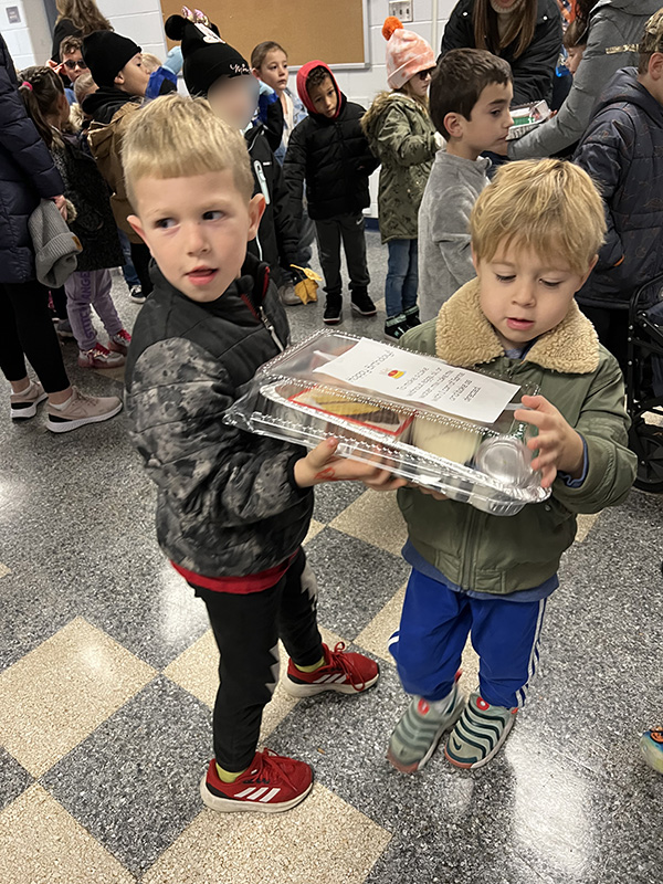 Two blonde kindergarten boys hold a tin with birthday cake makings in it.
