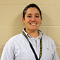 A woman with short dark hair, wearing a button-down shirt and a key lanyard around her neck smiles.