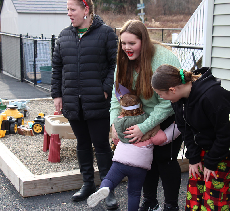 A little girl hugs the legs of a middle school girl.