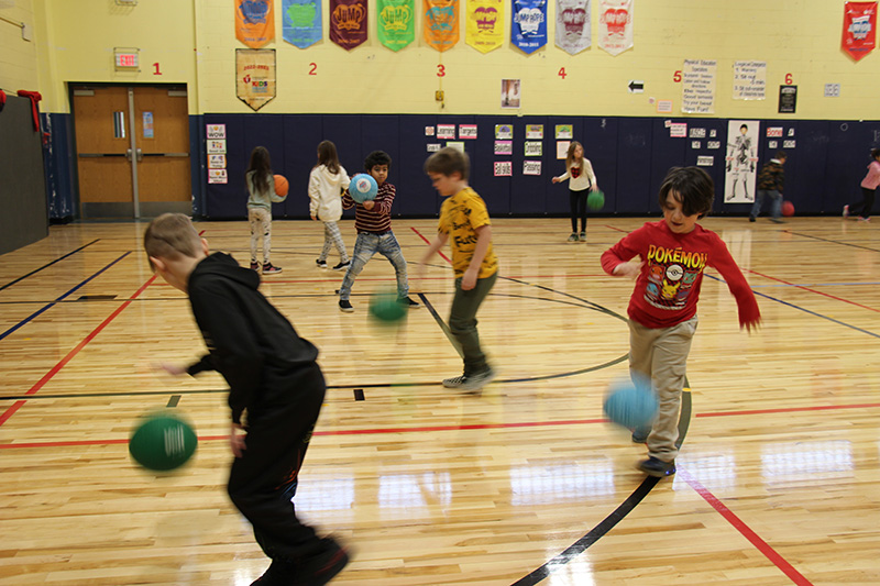 Several second-grade boys in a gym dribble basketballs.