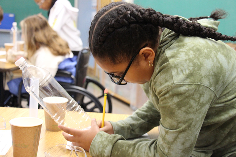 A third-grade girl looks at a temperature strip in a bottle and records the results.