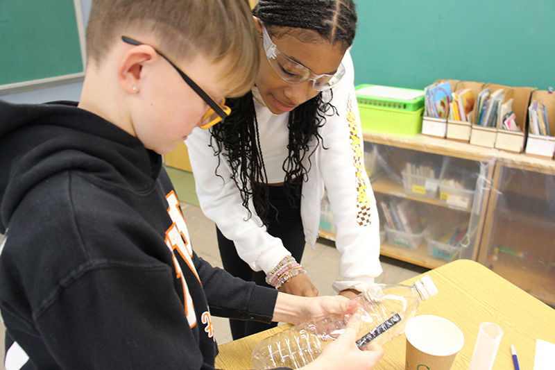 Two third graders look at the clear plastic bottle they are holding and noticing the temperature on the strip.