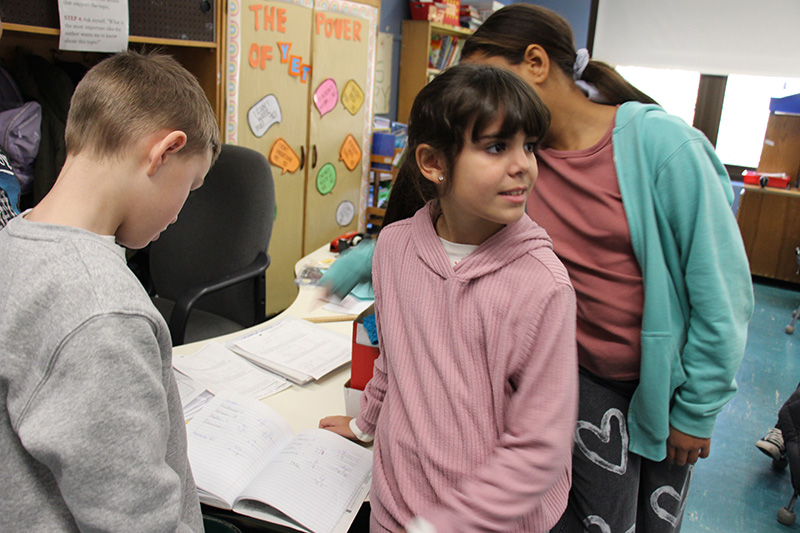 Fourth-grade students look in a notebook that has figures in it.