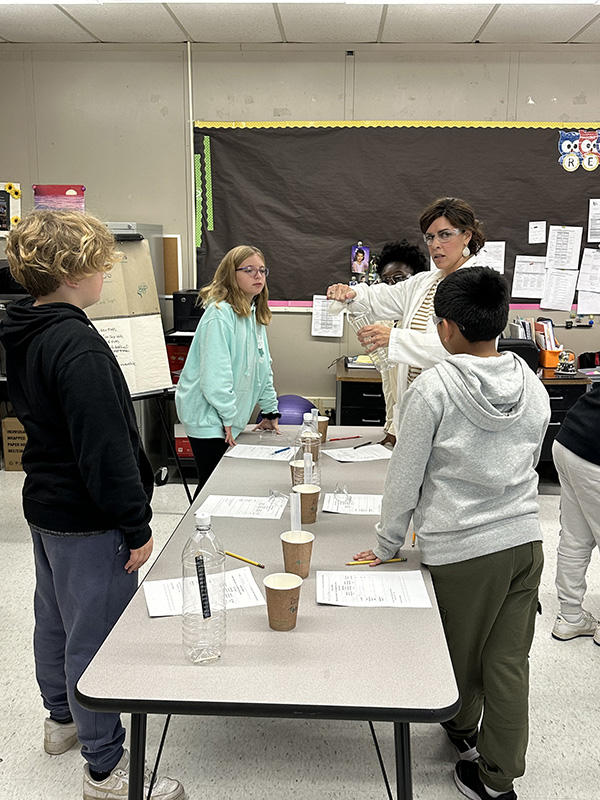 A woman shows a group of fifth-grade students instructions for a science project.