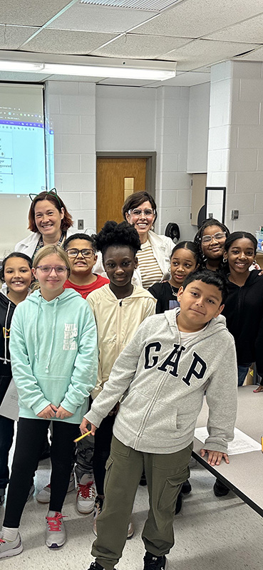 A group of right fifth-graders and two adults stand together and smile.