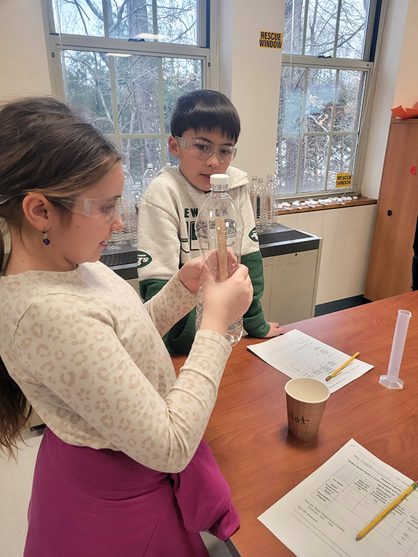Two fifth-grade students work on an experiment with a clear plastic bottle.