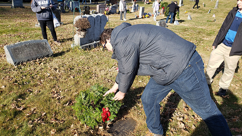 A young man places a green wreath on a grave.
