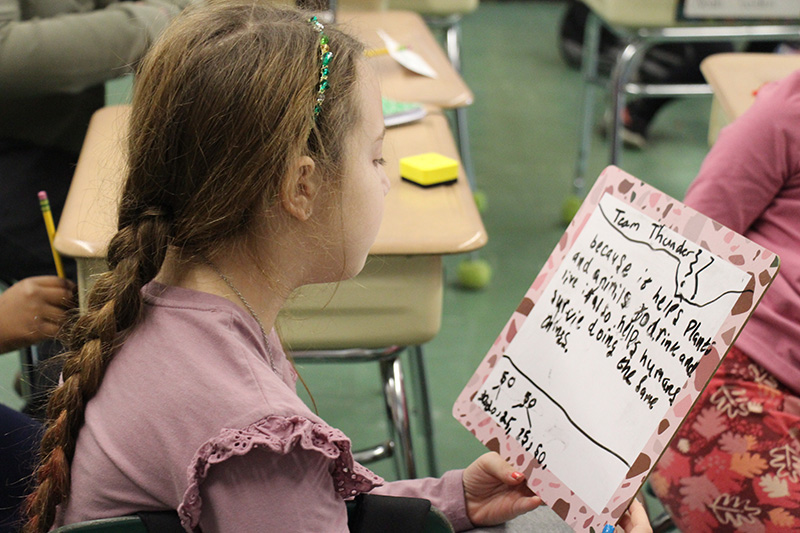 A third grade girl reads from a white board.