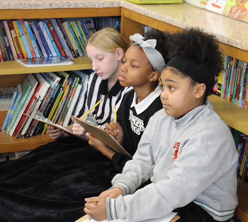 Three fifth-grade girls sit together and listen to a lecture.