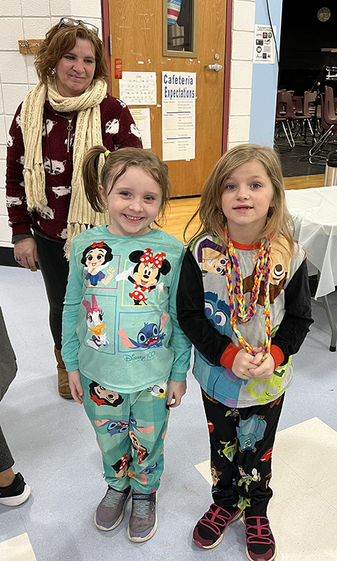 Two elementary age girls wearing comfy pajamas stand and smile.
