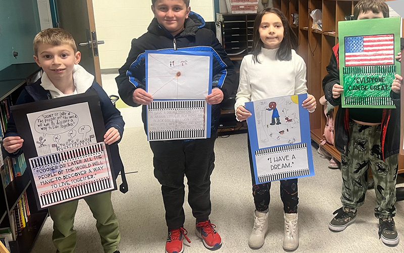 Four younger elementary students holding posters they made with American flags and pictures of Martin Luther King Jr. The students are smiling.