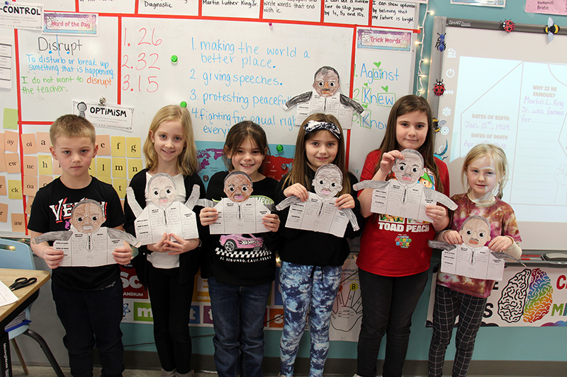 A group of six second-graders stand holding their pictures of Martin Luther King Jr.